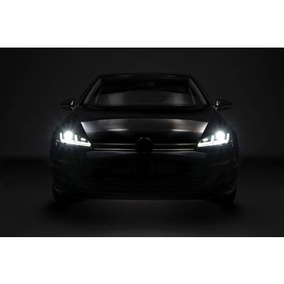 Ein Auto bei Nacht, frontal fotografiert, mit eingeschaltetem Abblendlicht, das die dunkle Umgebung beleuchtet.
