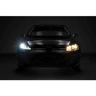 Ein Auto mit eingeschaltetem Abblend- und Fernlicht steht frontal in einem dunklen Raum.