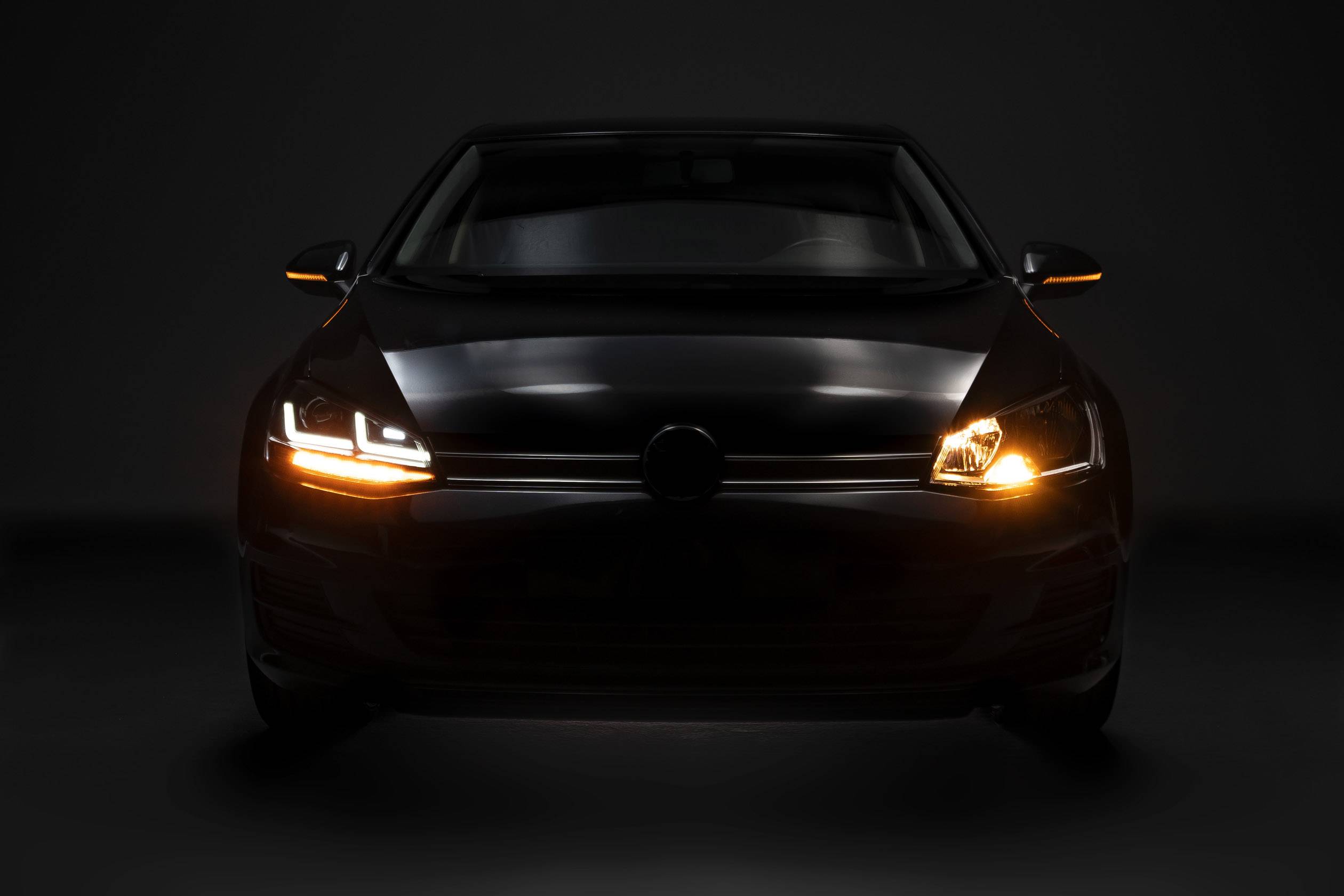 Ein Auto mit eingeschalteten Frontlichtern und Blinkern, frontal bei schwachem Licht fotografiert.