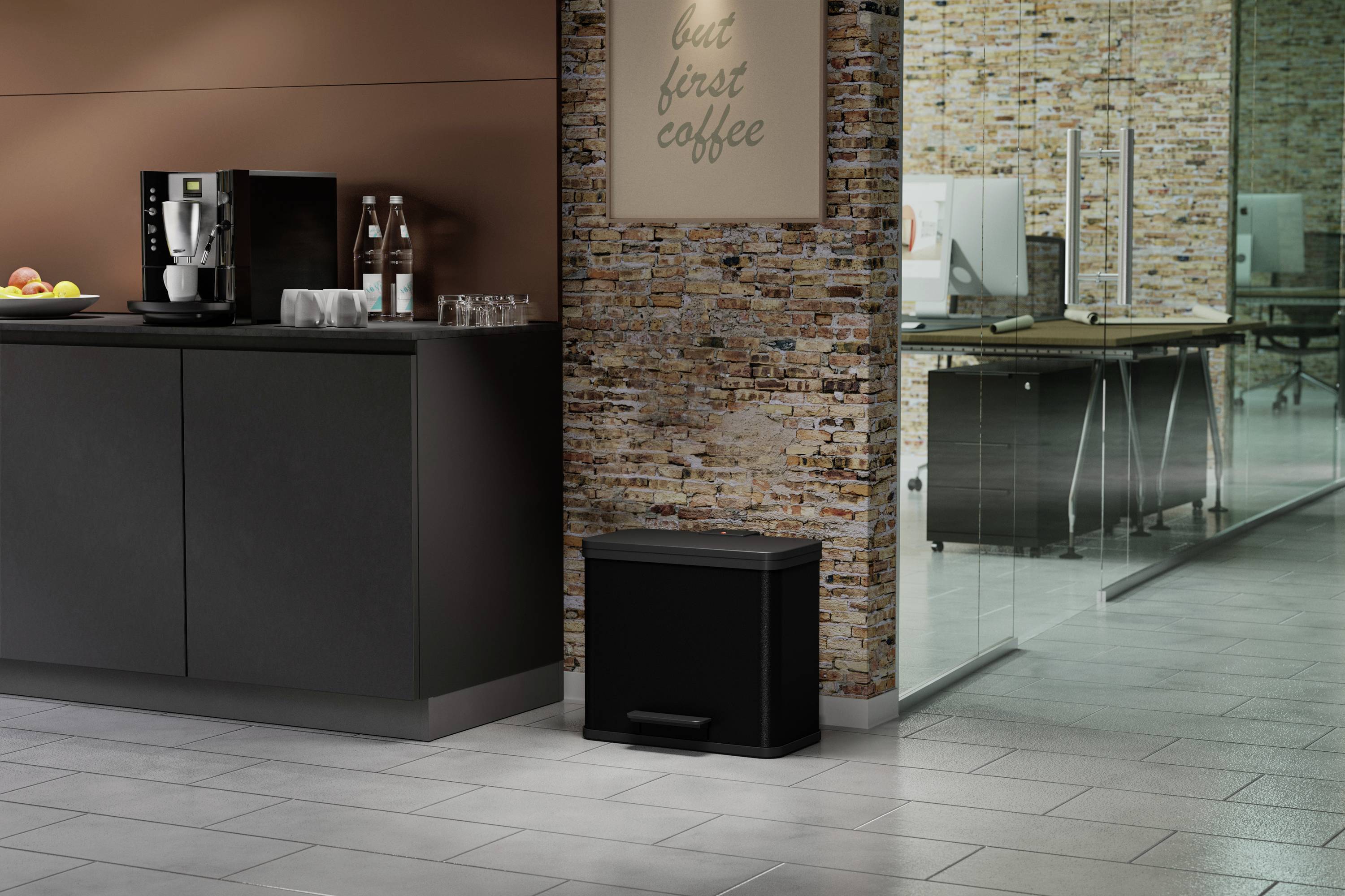 Eine moderne Büroküche mit Kaffeemaschine und Wasserspender auf einem schwarzen Schrank; daneben ein schwarzer Mülleimer. Im Hintergrund ist ein Glastisch zu sehen.