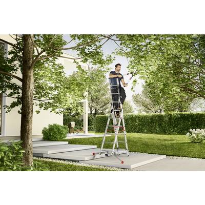 Mann steht auf einer Leiter und schneidet Äste in einem Garten vor einem modernen Haus.