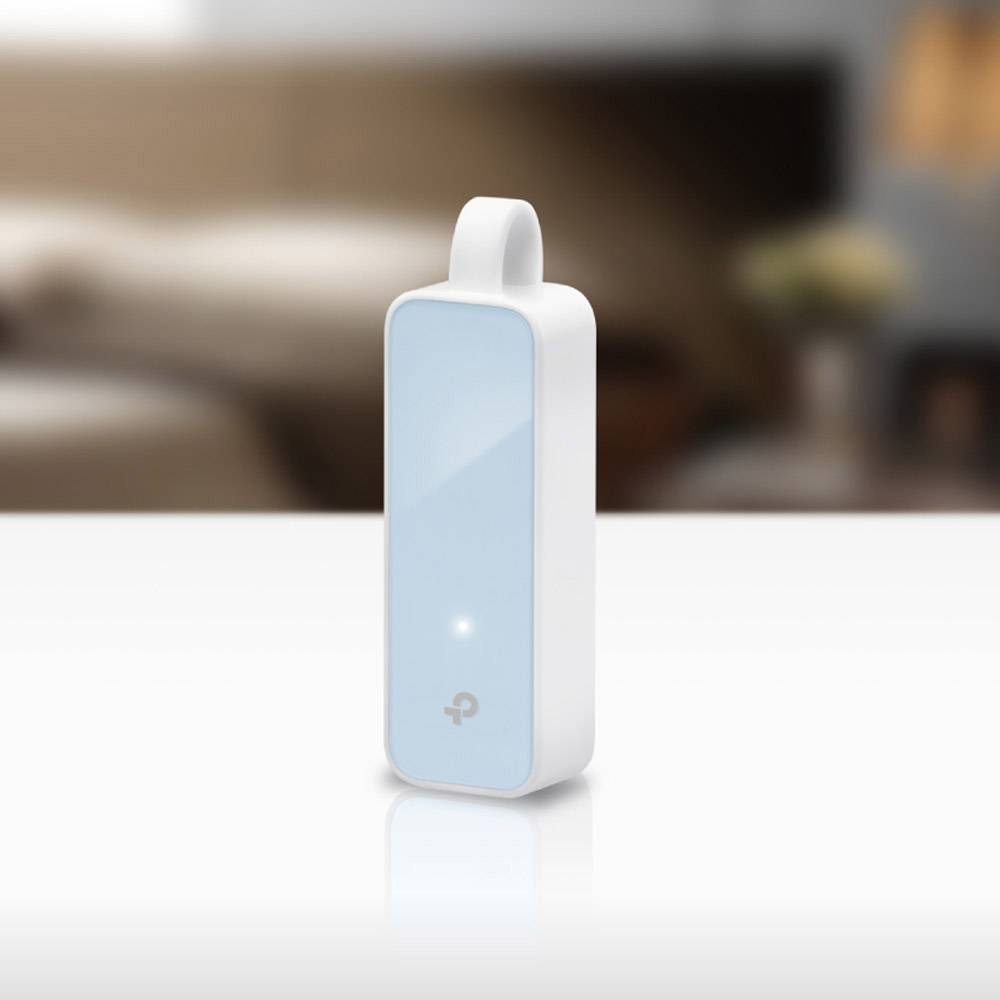 Ein weiß-blaues TP-Link USB-WLAN-Adaptergerät steht auf einem Tisch vor einem verschwommenen Wohnzimmerhintergrund.