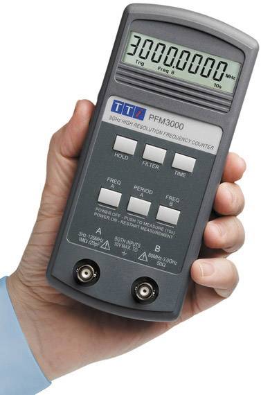 Hand hält digitales Frequenzmessgerät mit Anzeige von '3000.0000 MHz'. Gerät hat Tasten für 'Hold', 'Filter', 'Time', 'Freq A', 'Freq B'.