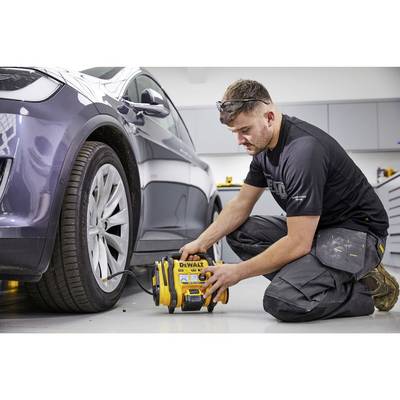 Ein Mann in Arbeitskleidung füllt mit einem tragbaren Luftkompressor die Reifen eines grauen Autos in einer Werkstatt auf.