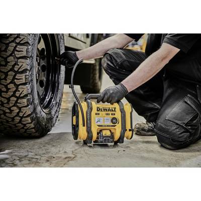 'Mann pumpt Autoreifen mit tragbarem Luftkompressor von DeWalt auf, trägt schwarze Hose und Handschuhe, im Freien.'