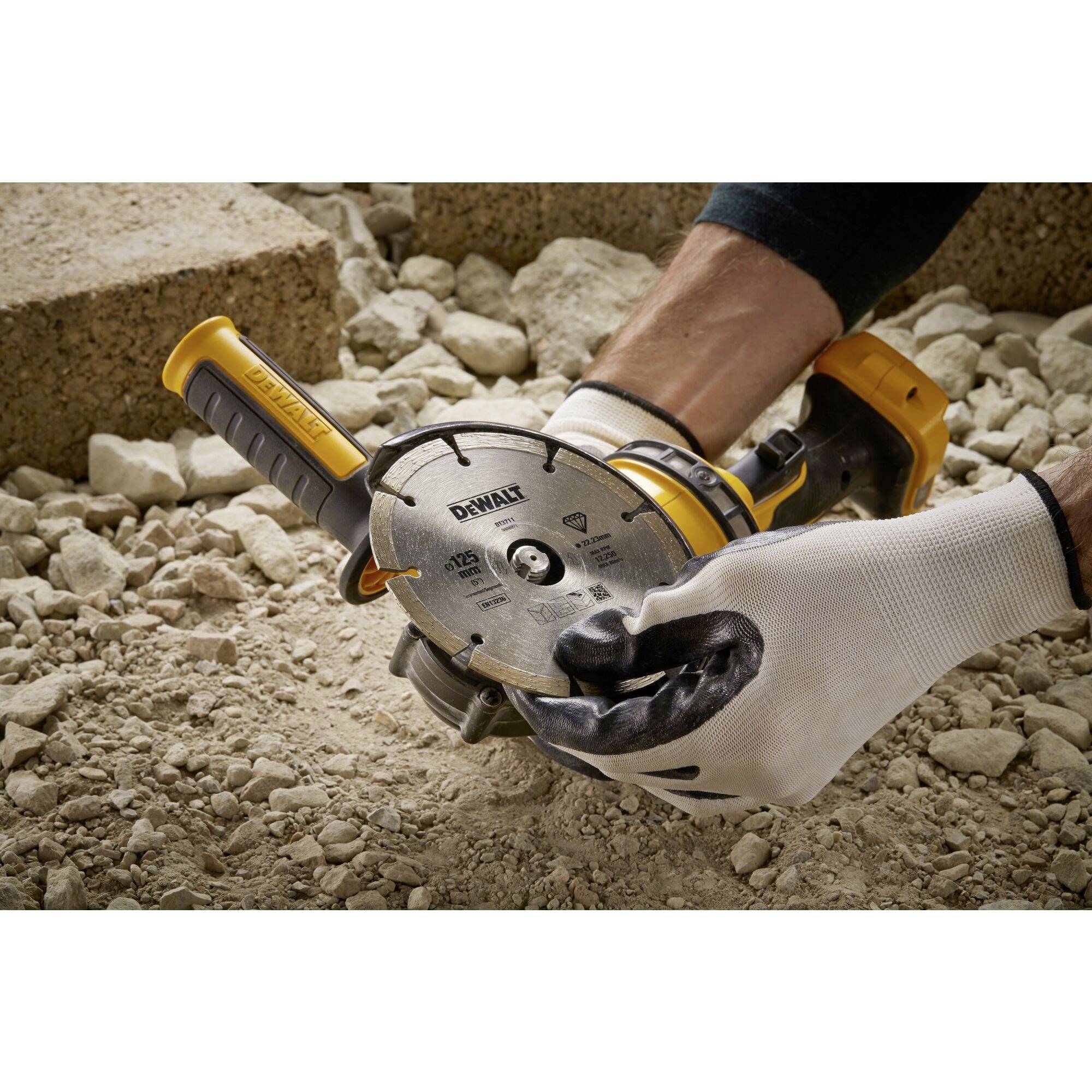 Ein Handwerker benutzt eine Kreissäge auf grobem Schotter. Er trägt Arbeitshandschuhe und hält die Säge sicher in der Hand.