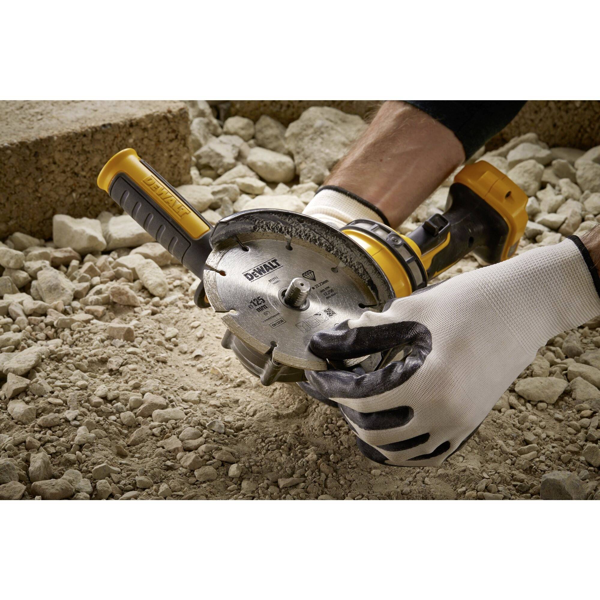 Person trägt Arbeitshandschuhe und hält eine Kreissäge. Werkzeug wird auf Baustelle verwendet, um Beton zu schneiden.