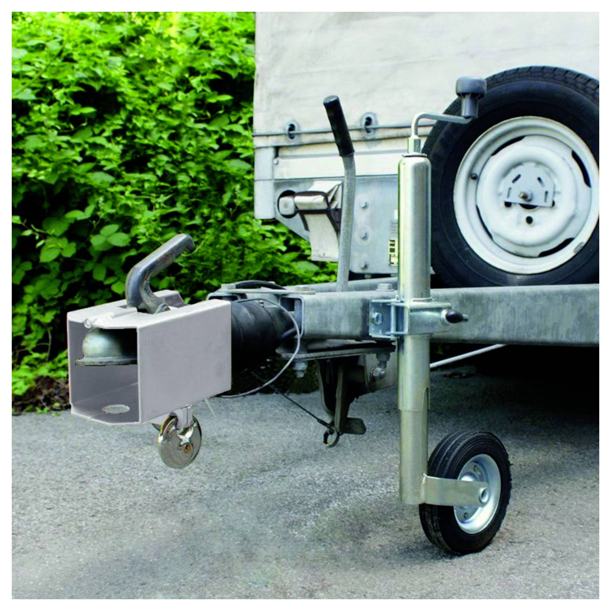 Eine Anhängerkupplung mit Anhängeschloss-System, geparkt auf Asphalt neben grünen Büschen.