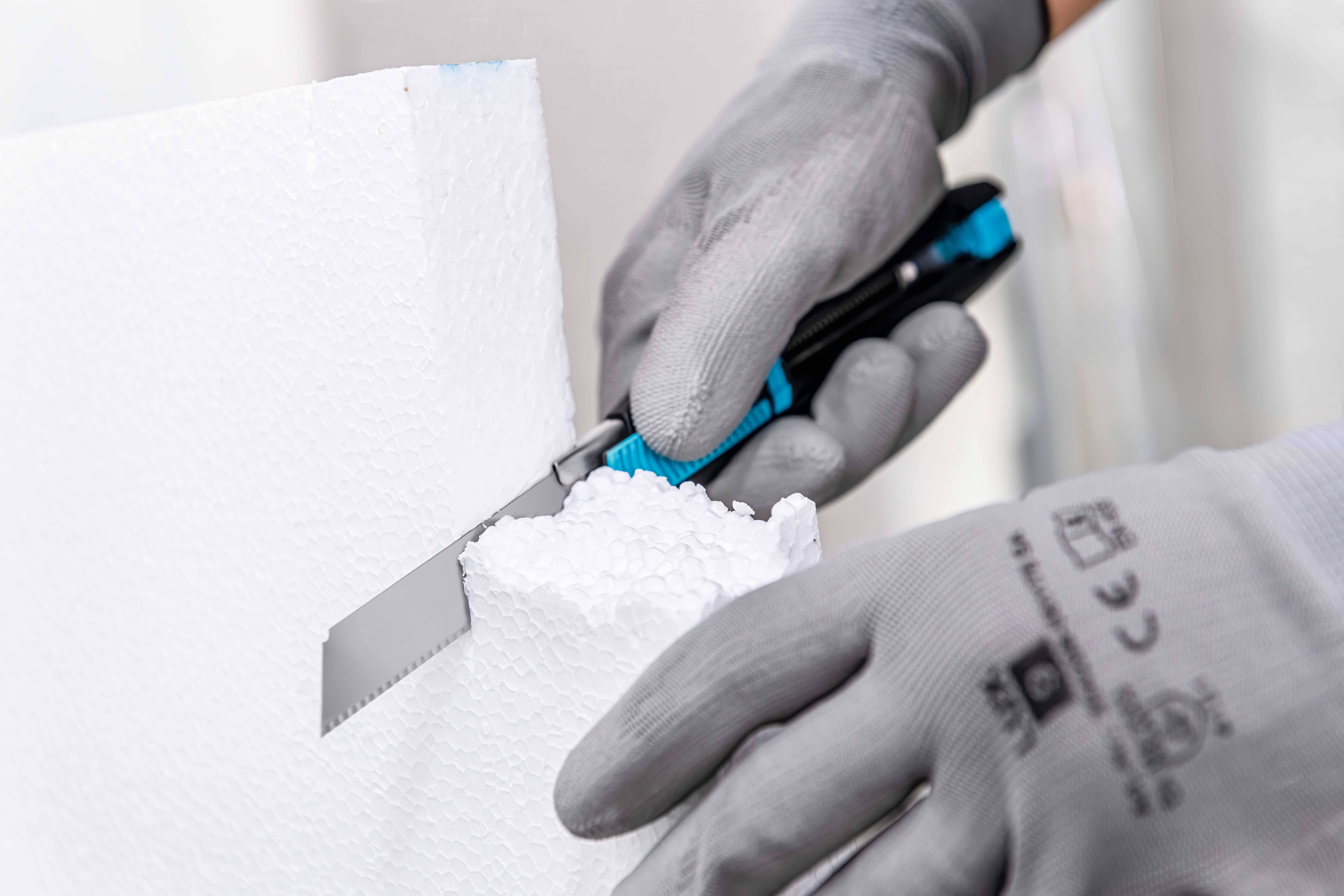 Eine Person schneidet mit einem kleinen Messer Styropor. Sie trägt graue Handschuhe, um die Hände zu schützen.