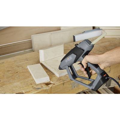 Eine Hand hält eine Heißklebepistole und klebt zwei Holzstücke in einem rechten Winkel auf einer Werkbank zusammen.