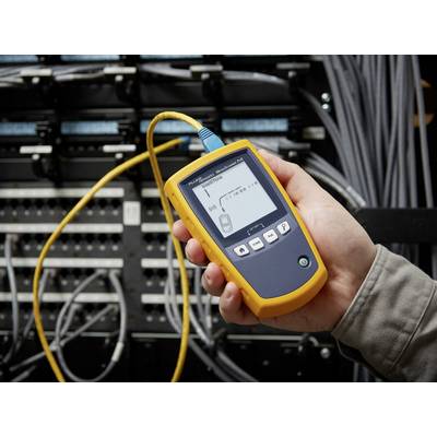 Eine Person hält ein Kabeltestgerät vor einem Netzwerk-Verteilerkasten. Das Display zeigt eine Kabelverbindungstestsituation an.