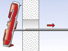 Eine rote Schraubstockklemme wird an einem durchbohrten Wandblock befestigt, eine Metallstange ragt durch eine Öffnung. Ein Pfeil zeigt die Richtung an.