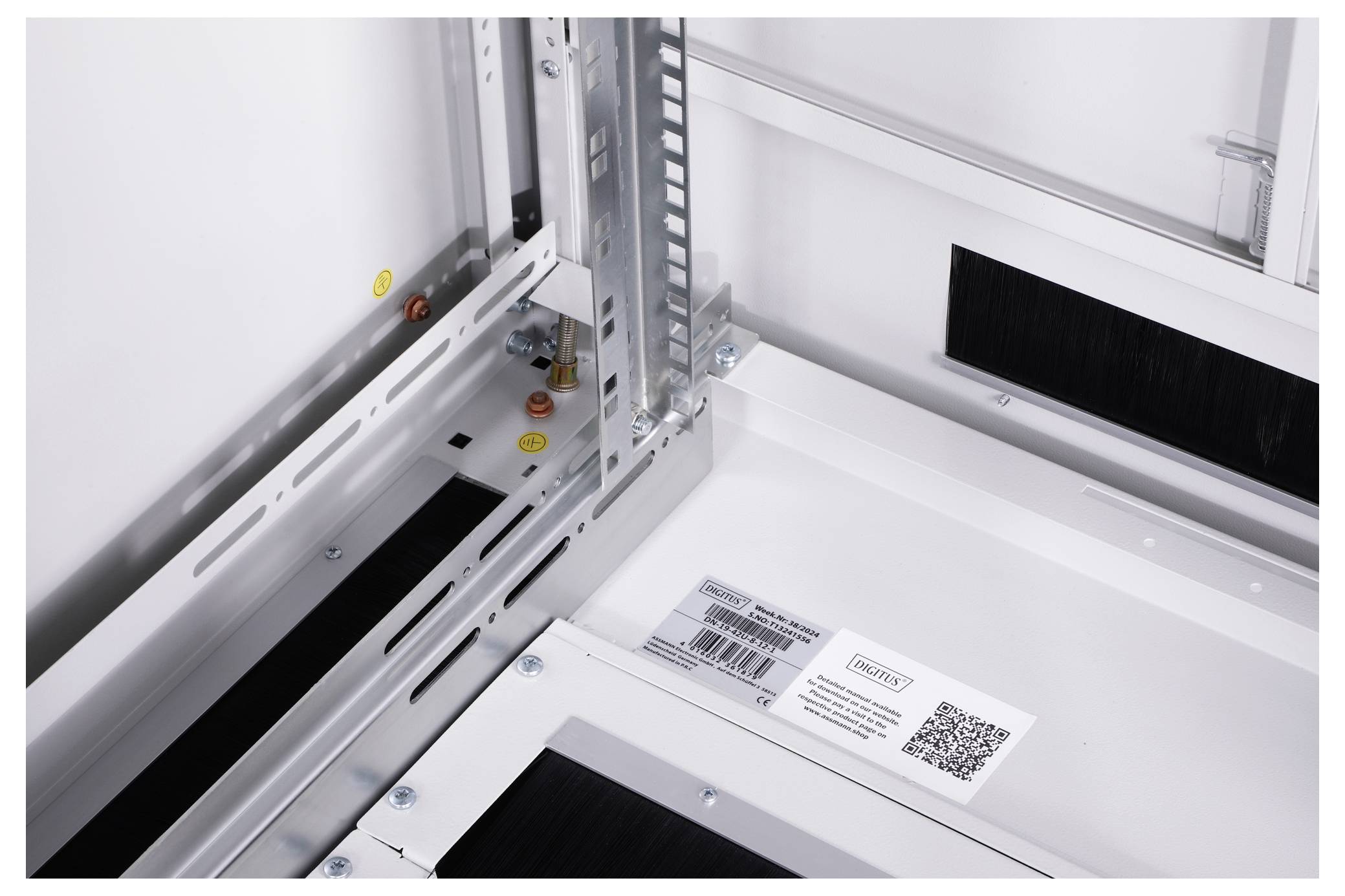 Detailansicht eines Serverracks mit Schienen zur Befestigung, Schrauben und Kabelmanagement. Ein QR-Code und Barcode sind sichtbar.