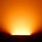 Ein heller, orangefarbener Schein strahlt von einer Lampe aus und verbreitet warmes Licht in einem dunklen Raum.