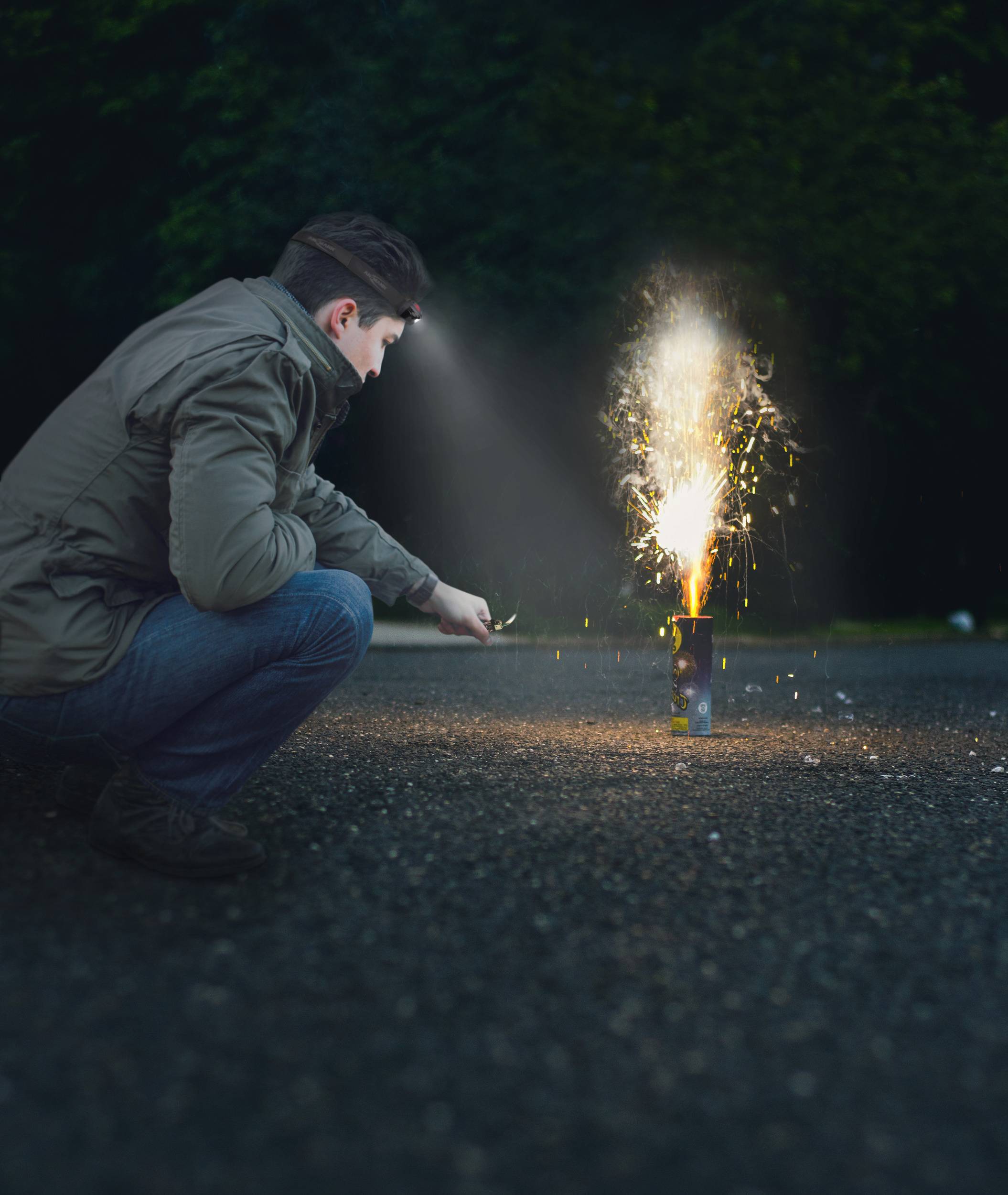 Eine Person zündet bei Dunkelheit ein Feuerwerk an; Funken fliegen. Sie trägt eine Stirnlampe. Im Hintergrund sind Bäume.
