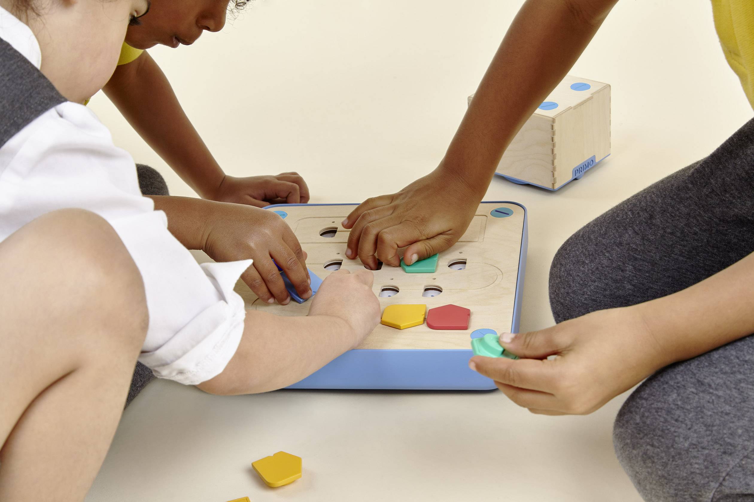 Drei Kinder spielen mit einem Holzspielzeug, das aus verschiedenen bunten Formen besteht. Sie passen die Formen in die entsprechenden Öffnungen ein.