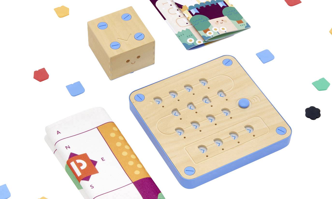 Holzspielzeug-Set mit verschiedenen geometrischen Formen und Farben, darunter ein Würfel, ein Spielbrett und bunte Kärtchen.