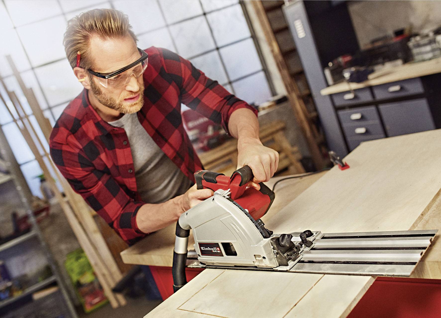 Ein Mann in einem Holzatelier schneidet mit einer Kreissäge Holz. Er trägt Schutzbrille und kariertes Hemd.