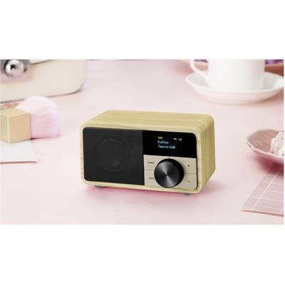 Ein kleines Holzradio steht auf einem rosa Tisch. Das Display zeigt 'Kaffee' und 'Time to Chill'. Daneben steht eine Tasse.