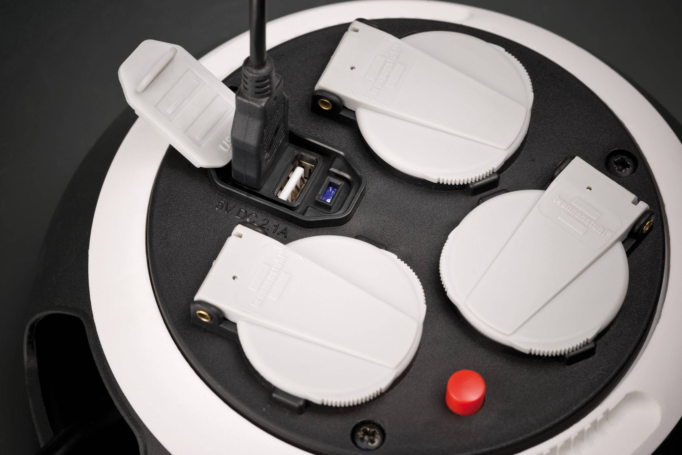 'Weiße Steckdosenleiste mit drei runden Steckdosen, USB-Anschluss und rotem Schalter. Ein USB-Kabel ist angeschlossen.'