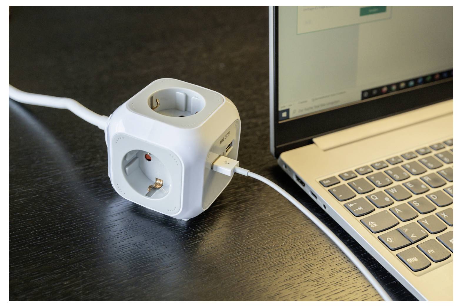 Weißer Würfel-Stromadapter mit mehreren Steckdosen und eingesteckten Kabeln neben einem Laptop auf einem Schreibtisch