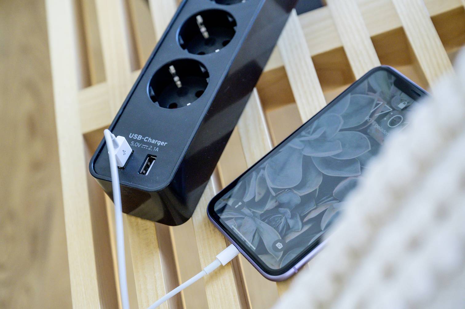 Smartphone lädt an einer Steckdosenleiste mit USB-Anschluss auf, positioniert auf einem Holztisch.