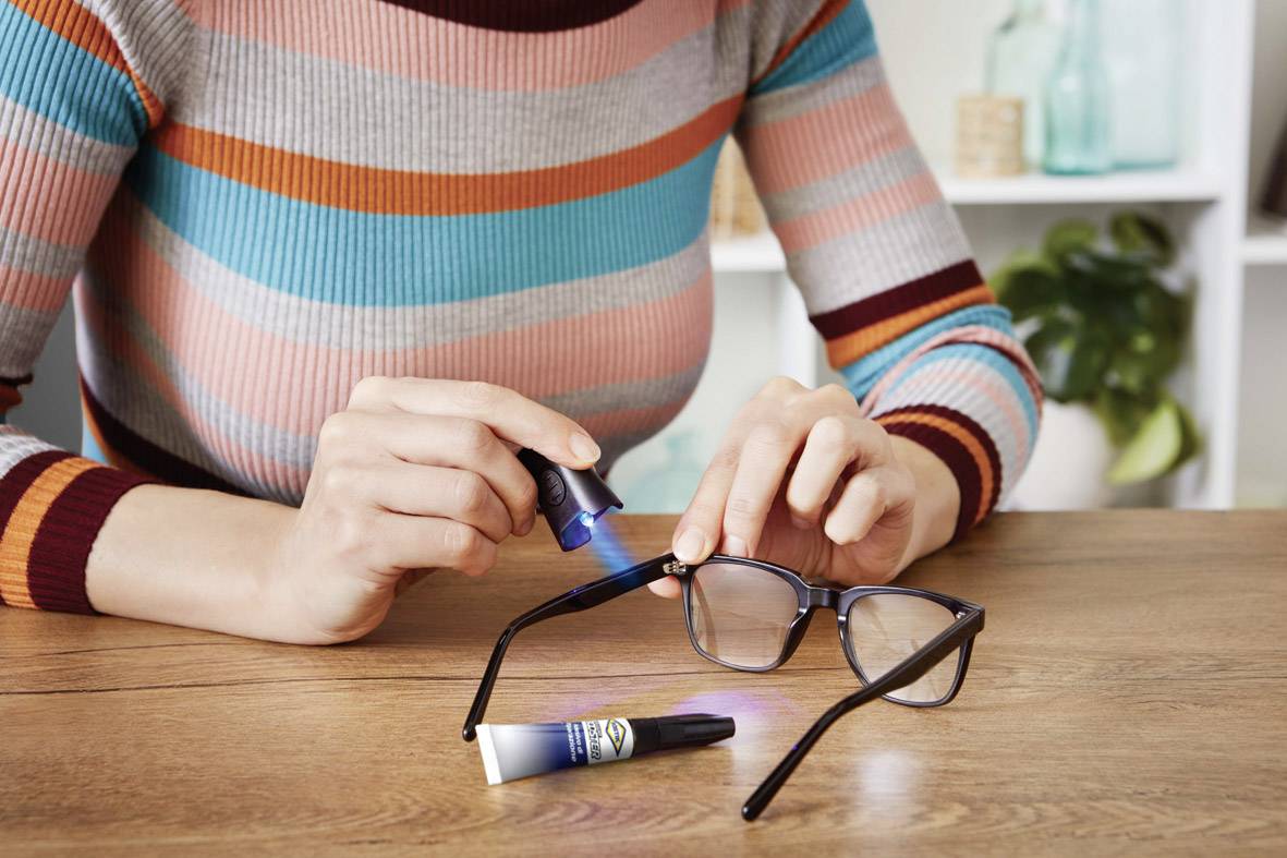 Person repariert eine Brille mit UV-Kleber, indem sie das Gestell an der Bruchstelle mit einer Lampe aushärtet.
