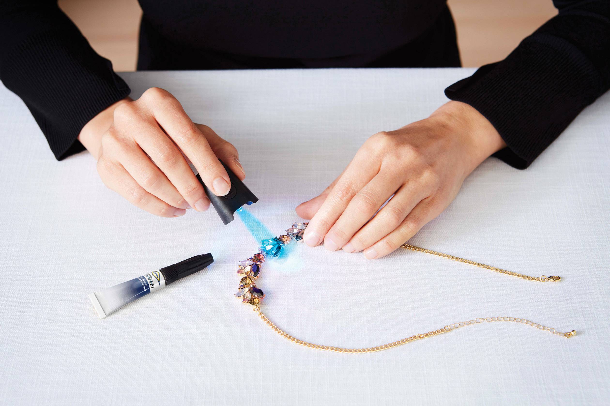 Person klebt Schmuck mit UV-Licht und Kleber; zeigt handwerkliche Reparaturarbeit.