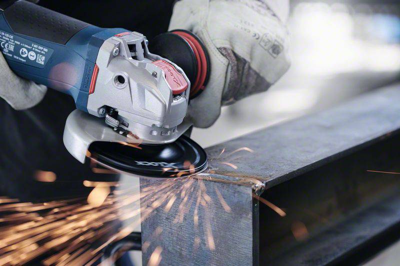 Ein Arbeiter in Handschuhen schleift mit einem Winkelschleifer Metall, dabei sprühen Funken vom bearbeiteten Material.