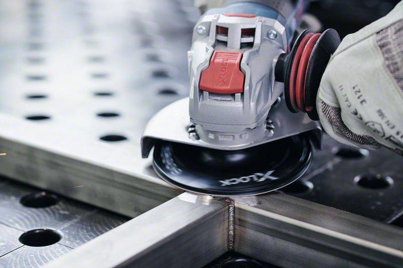 Eine Person schleift mit einem Winkelschleifer Metall auf einem Tisch mit Löchern. Funken sprühen vom Metallrand.