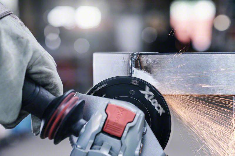 Eine Person schleift den Rand eines Metallobjekts mit einem Winkelschleifer. Funken fliegen vom Objekt weg.