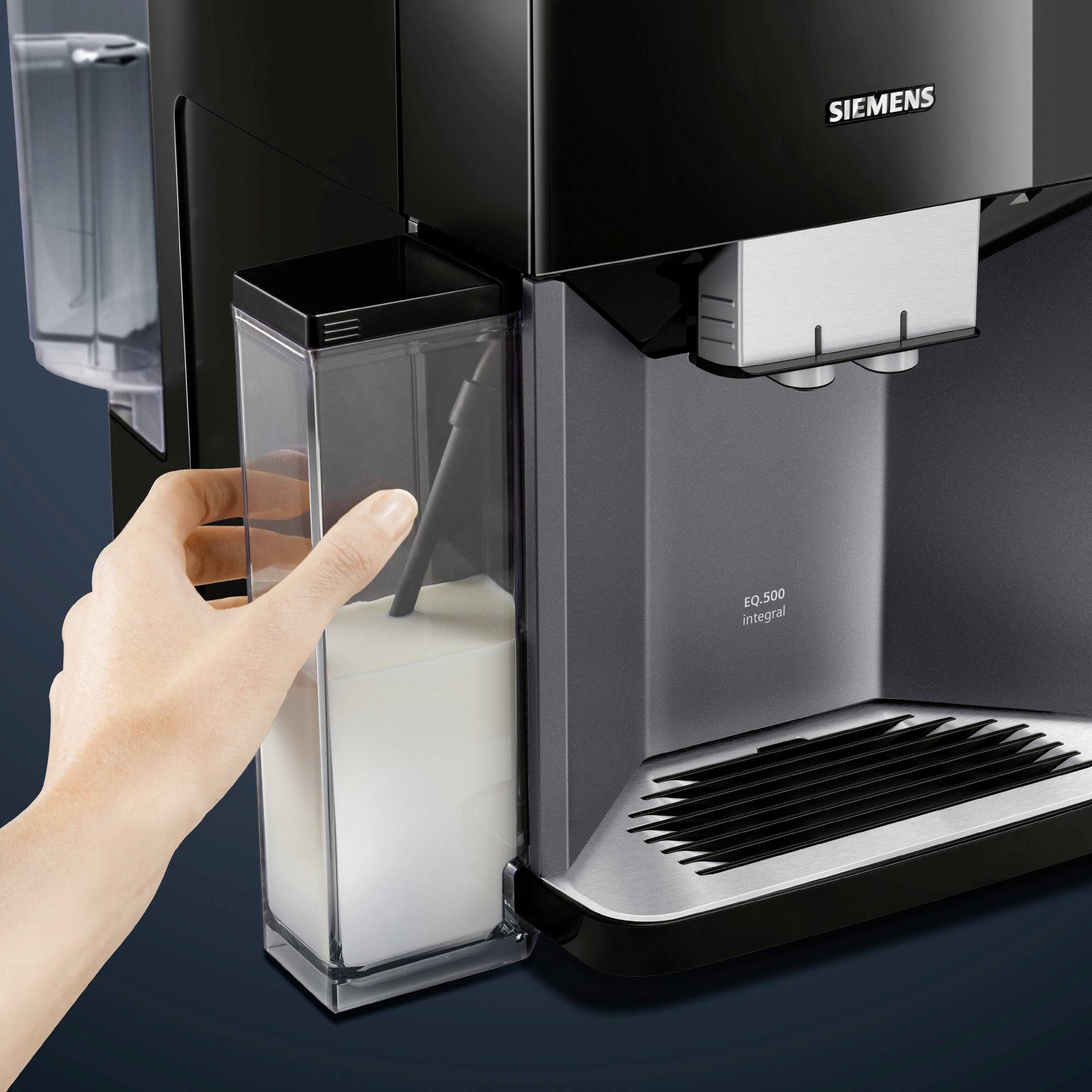 Eine Hand hält ein Gehäuse mit Milch neben einer schwarzen Siemens EQ.500 Kaffeemaschine, zur Herstellung von Kaffee.