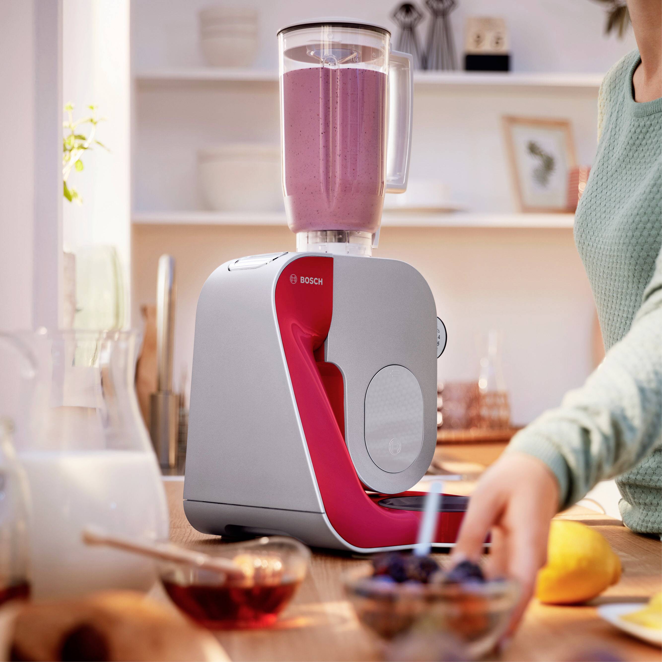 Eine Person bereitet einen Smoothie mit einem Standmixer in einer hellen Küche zu. Daneben liegt eine halbe Zitrone auf der Arbeitsfläche.