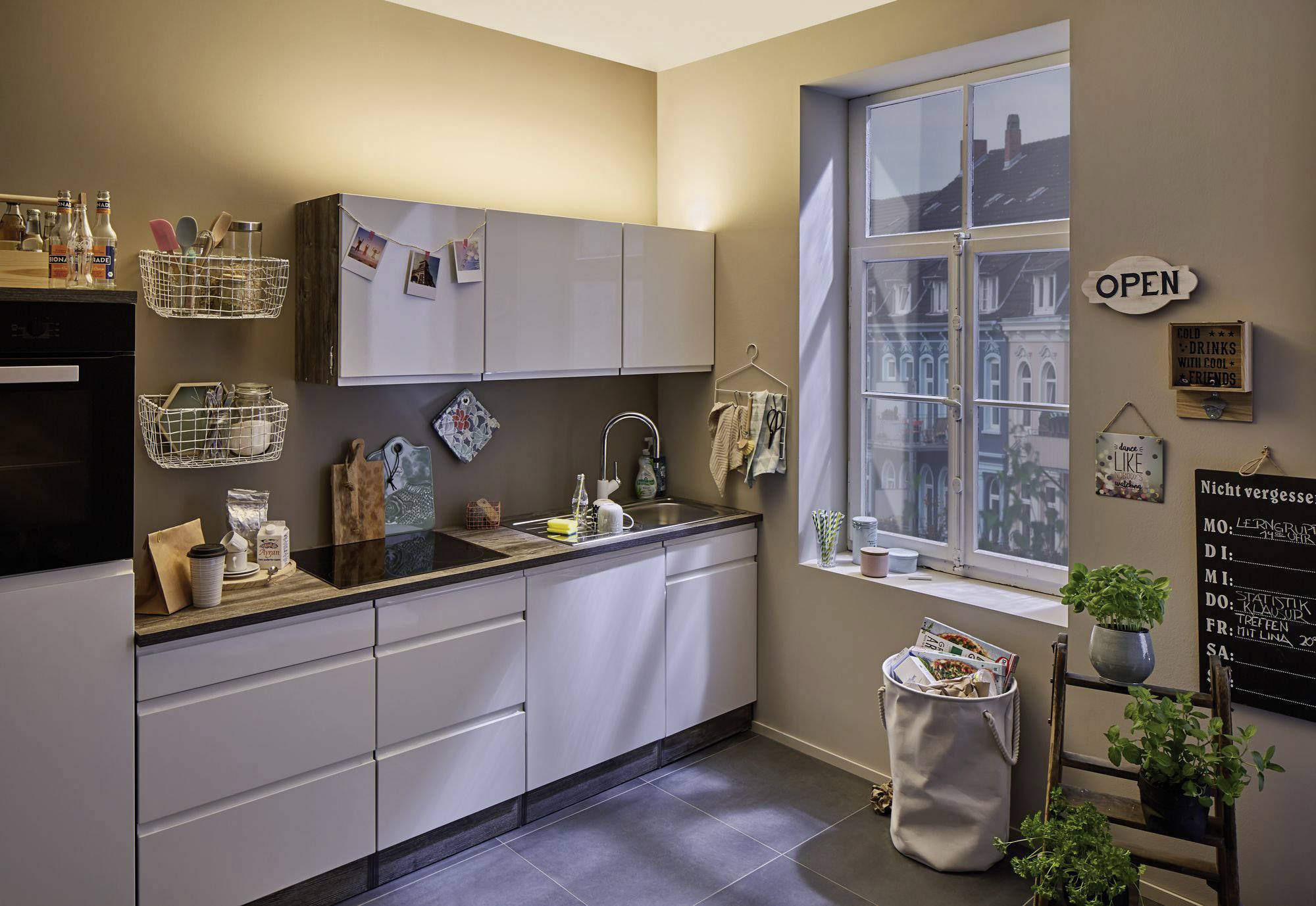 Moderne Küche mit weißen Schränken, einem Waschbecken und einem großen Fenster. Helle Beleuchtung und diverse Dekorationen.