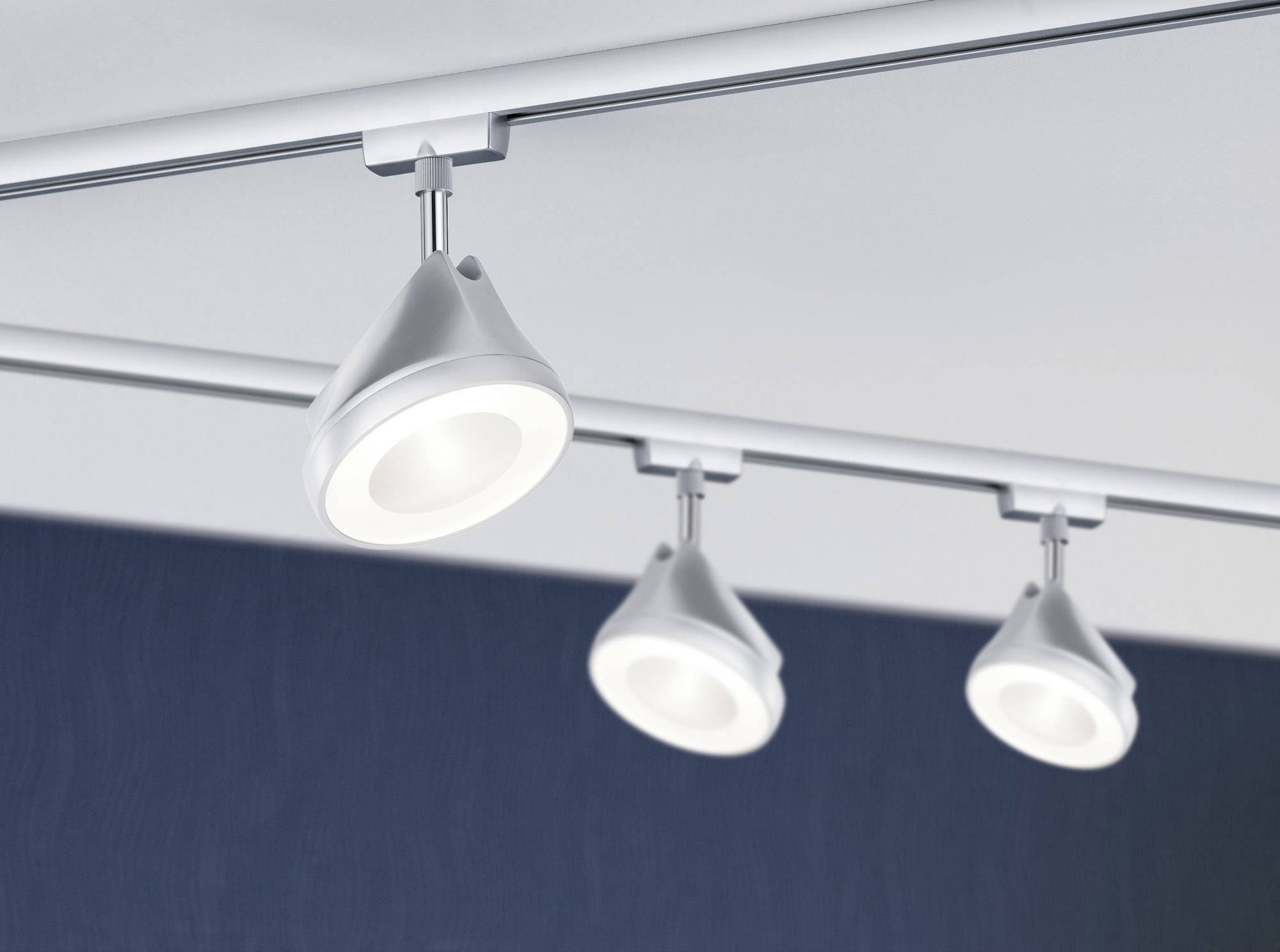 Drei moderne, weiße Deckenstrahler an einer Schiene montiert, leuchten gleichmäßig in einem Innenraum mit dunkelblauer Wand.