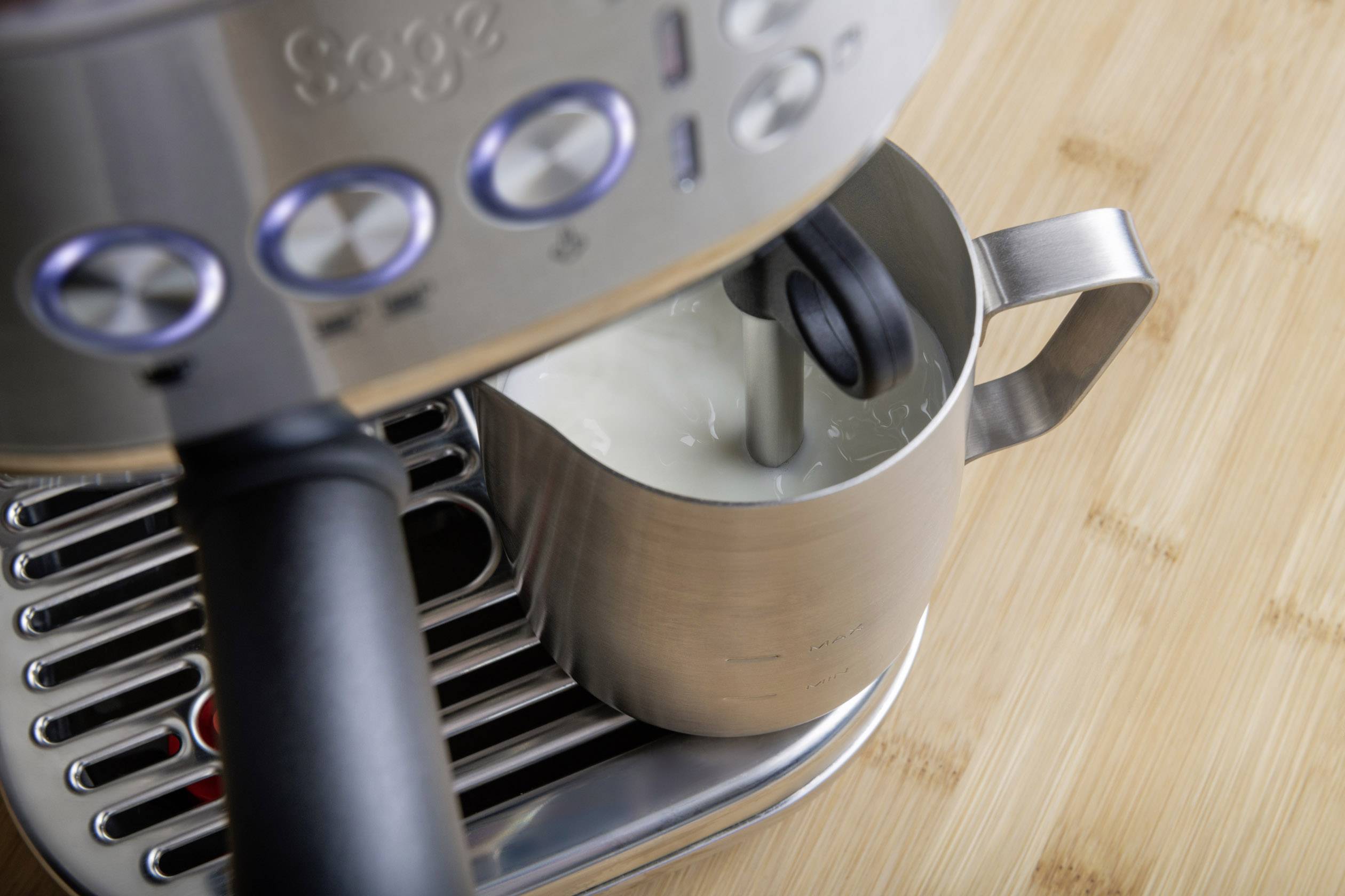 Milch wird mit einem automatischen Dampfstab in einer Edelstahlkanne aufgeschäumt, die auf einer Espressomaschine steht.