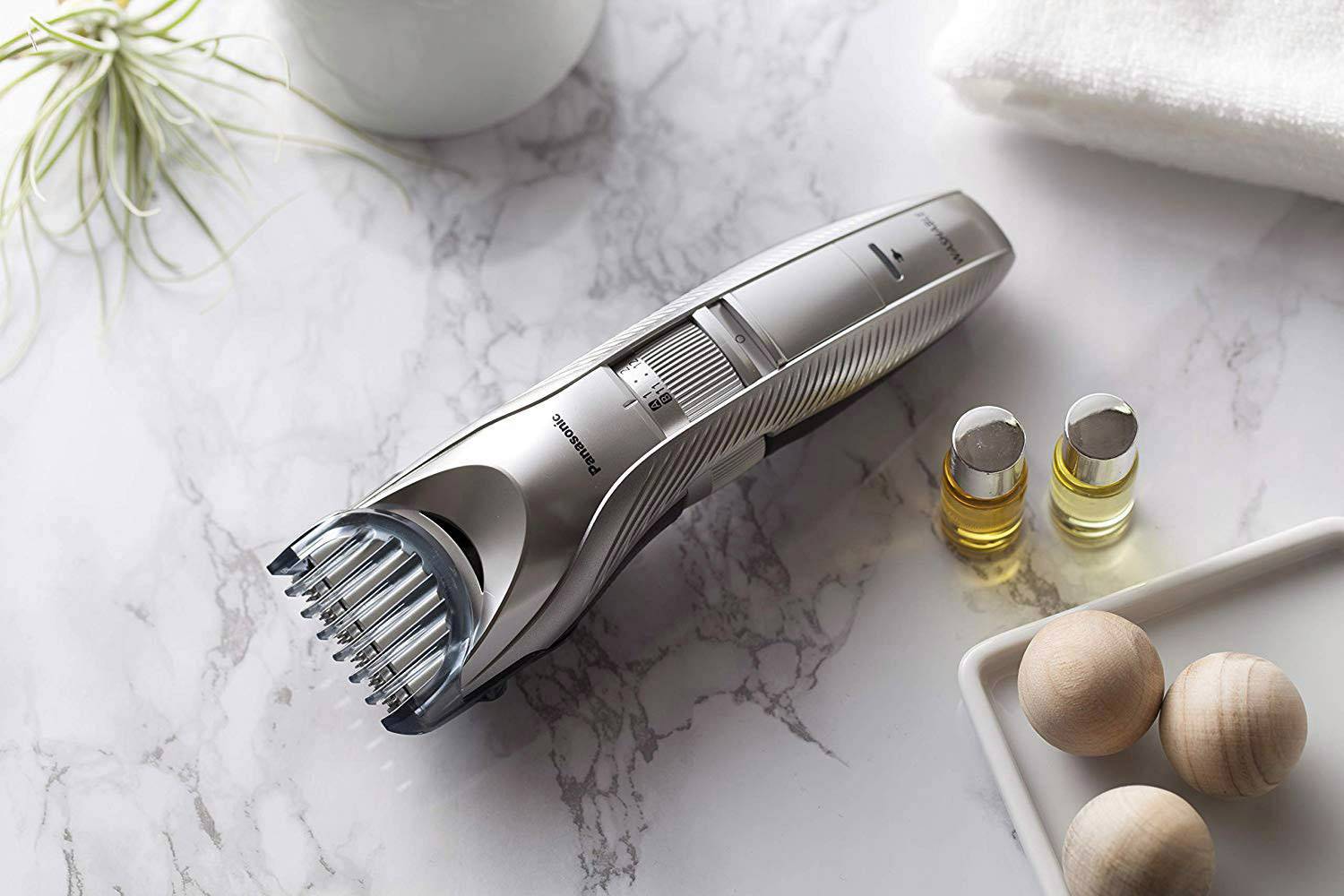 Elektrischer Rasierer auf Marmorplatte, daneben kleine Fläschchen mit Öl, Holzperlen und ein Handtuch.