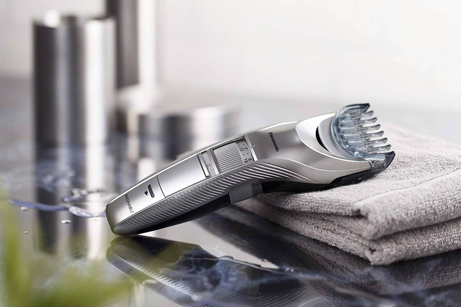 Ein silberner elektrischer Haarschneider liegt auf einem gefalteten grauen Handtuch. Im Hintergrund sind unscharfe Formen sichtbar.