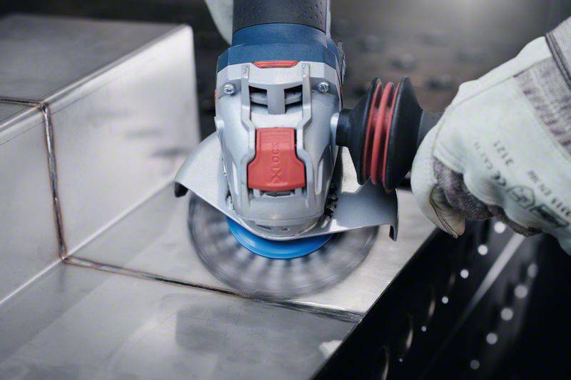 Eine Person bearbeitet eine Metalloberfläche mit einem Winkelschleifer. Der Funkenflug zeigt die Materialabtragung beim Schleifen.