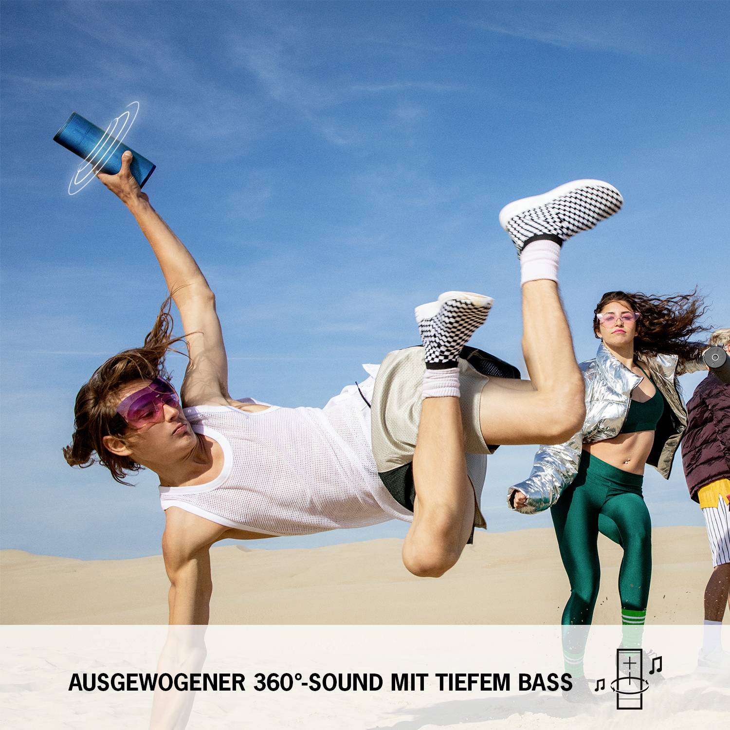 Junge Leute tanzen energiegeladen am Strand in heller Kleidung. Unten steht: 'Ausgewogener 360°-Sound mit tiefem Bass'.