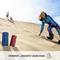 Eine Frau fährt auf einem Sandboard eine Düne hinunter. Zwei Lautsprecher stehen im Sand. Text: 'Sturzfest + geschützt gegen Staub'.