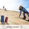Eine Frau gleitet auf einem Sandboard eine Düne hinunter. Zwei Lautsprecher im Vordergrund, beschriftet mit 'Drop Proof + Dust Proof'.