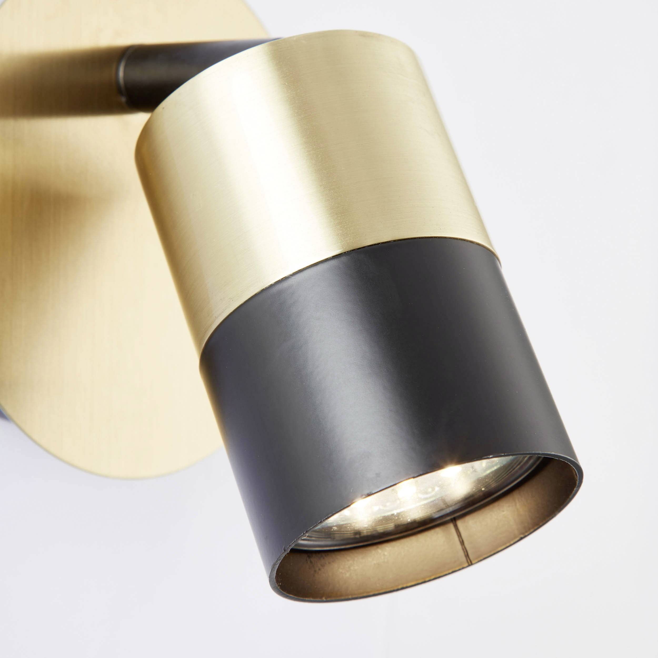 Eine moderne Wandleuchte aus gebürstetem Metall mit einem zylindrischen Lampenschirm in Gold und Schwarz.