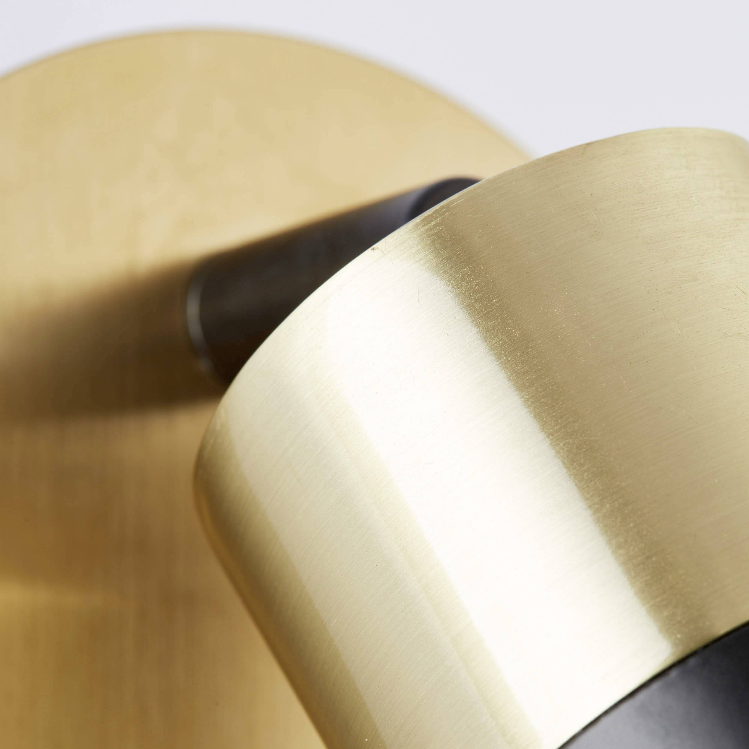 Nahaufnahme einer goldenen, zylindrischen Wandleuchte, die leicht geneigt ist, vor einem neutralen Hintergrund.