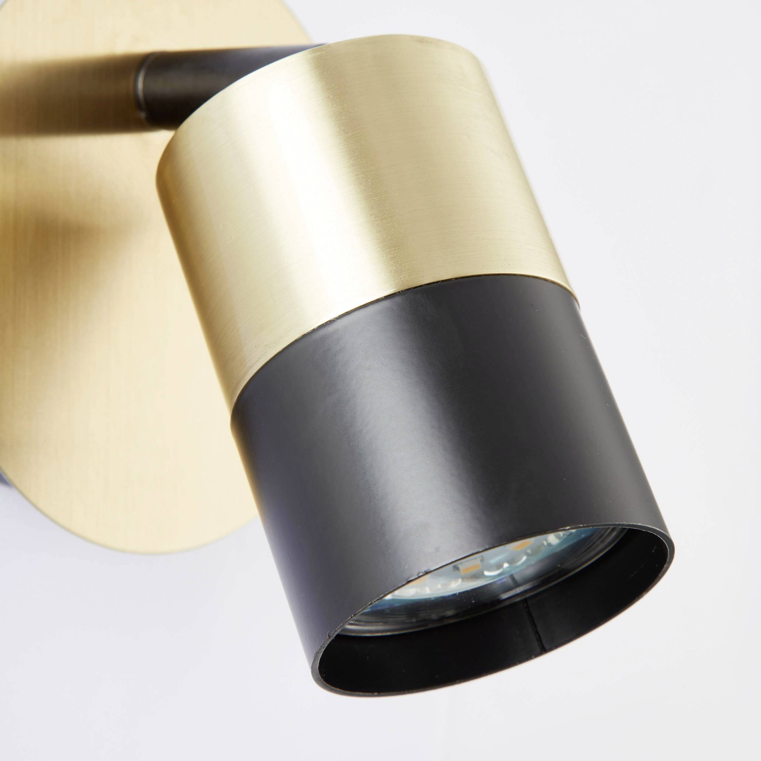 Eine moderne Wandleuchte mit zylindrischem, zweifarbigem Design in Schwarz und Messing, montiert auf einer runden Platte.