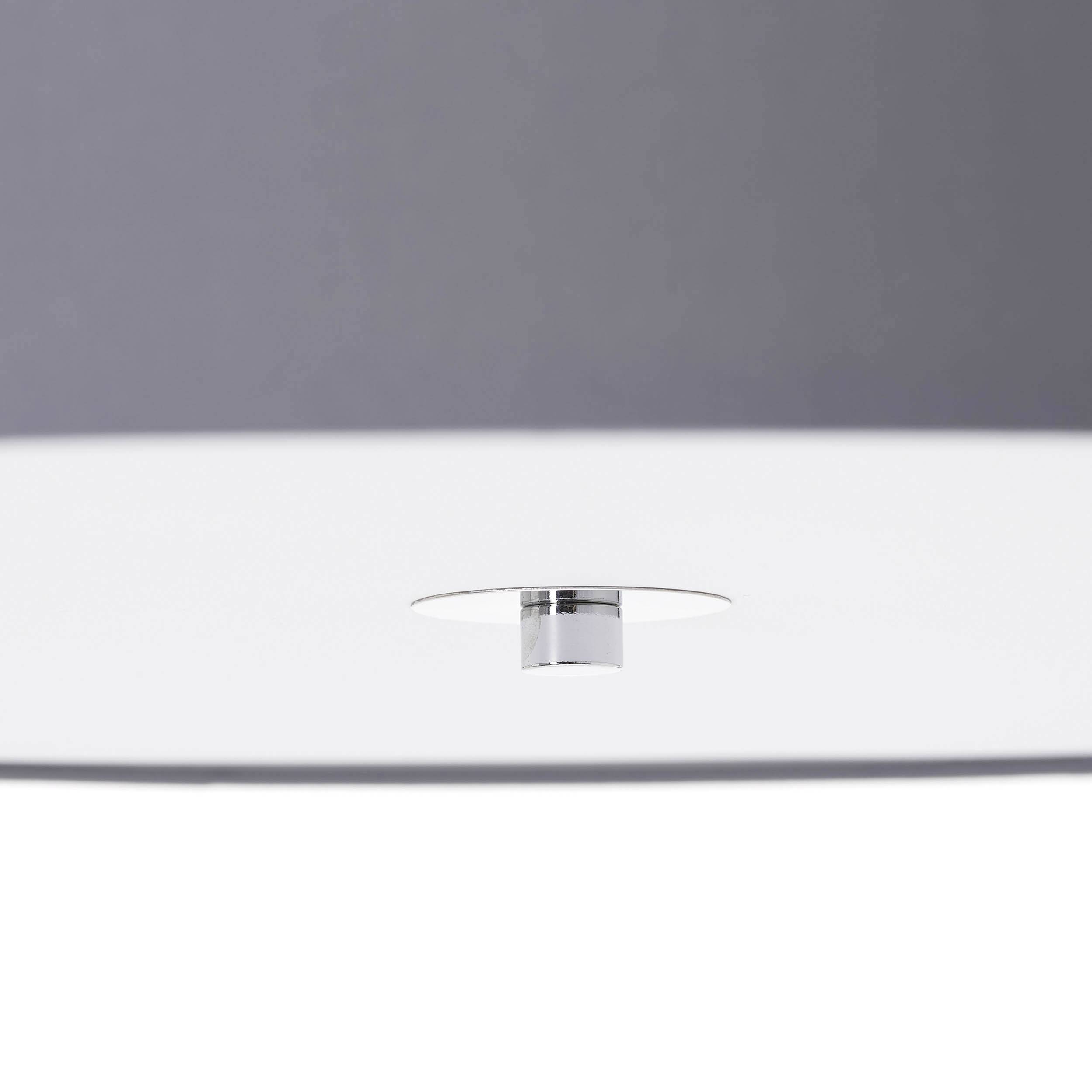 Eine weiße, minimalistische Deckenleuchte mit einem kleinen, zentralen, metallischen Verbindungselement vor grauem Hintergrund.