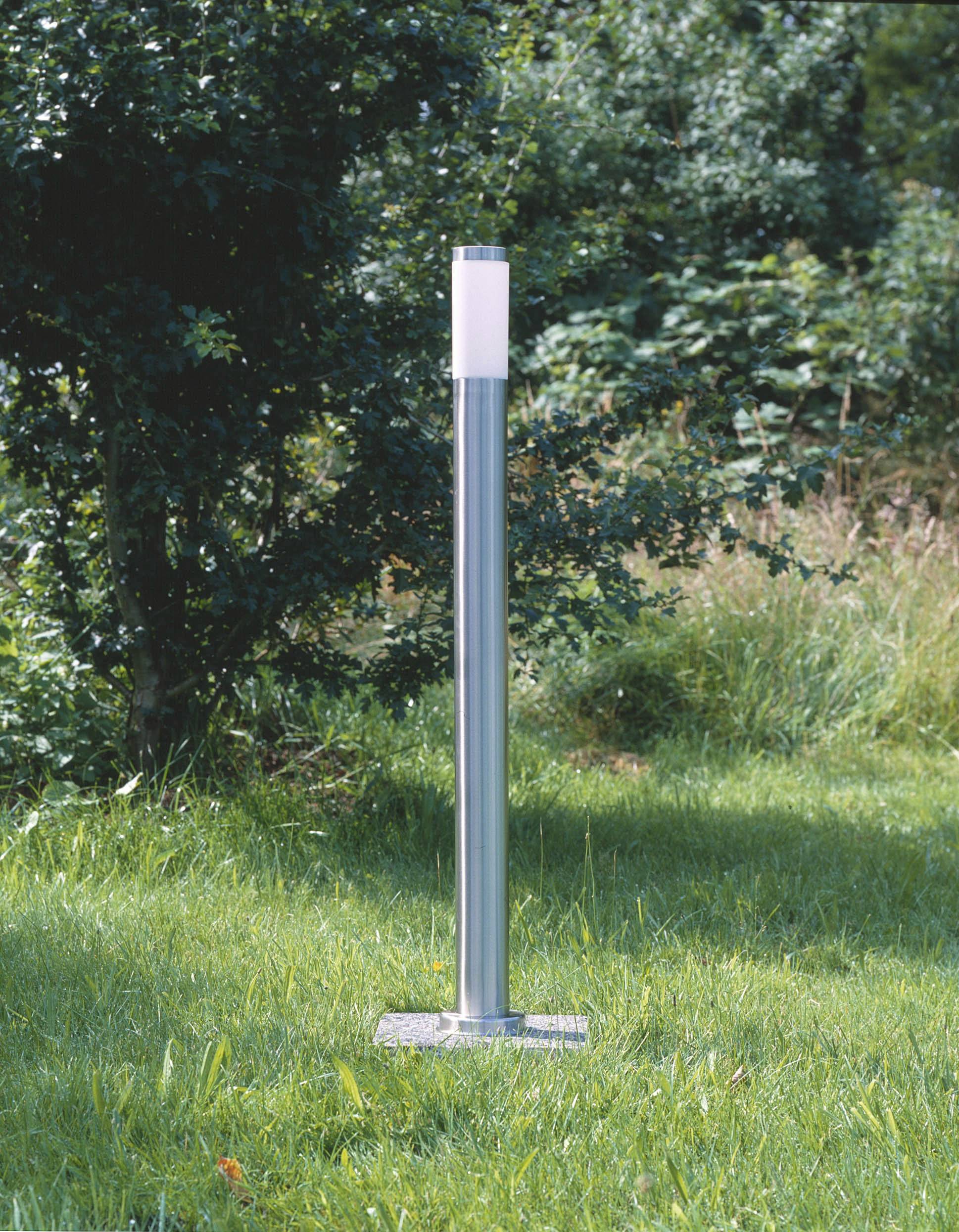 Eine moderne, silberne Außenlampe steht auf einer grünen Rasenfläche, umgeben von Bäumen im Hintergrund.