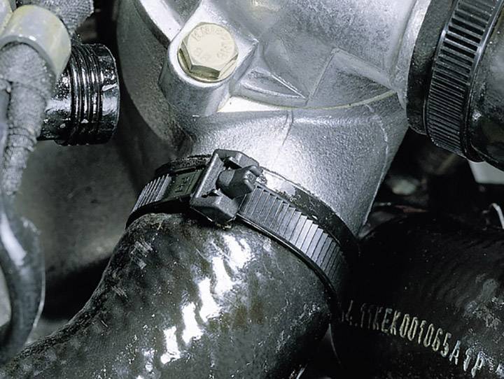 Ein schwarzer Kabelbinder sichert einen schwarzen Gummischlauch an einem silbernen Metallventil in einem Motorraum.