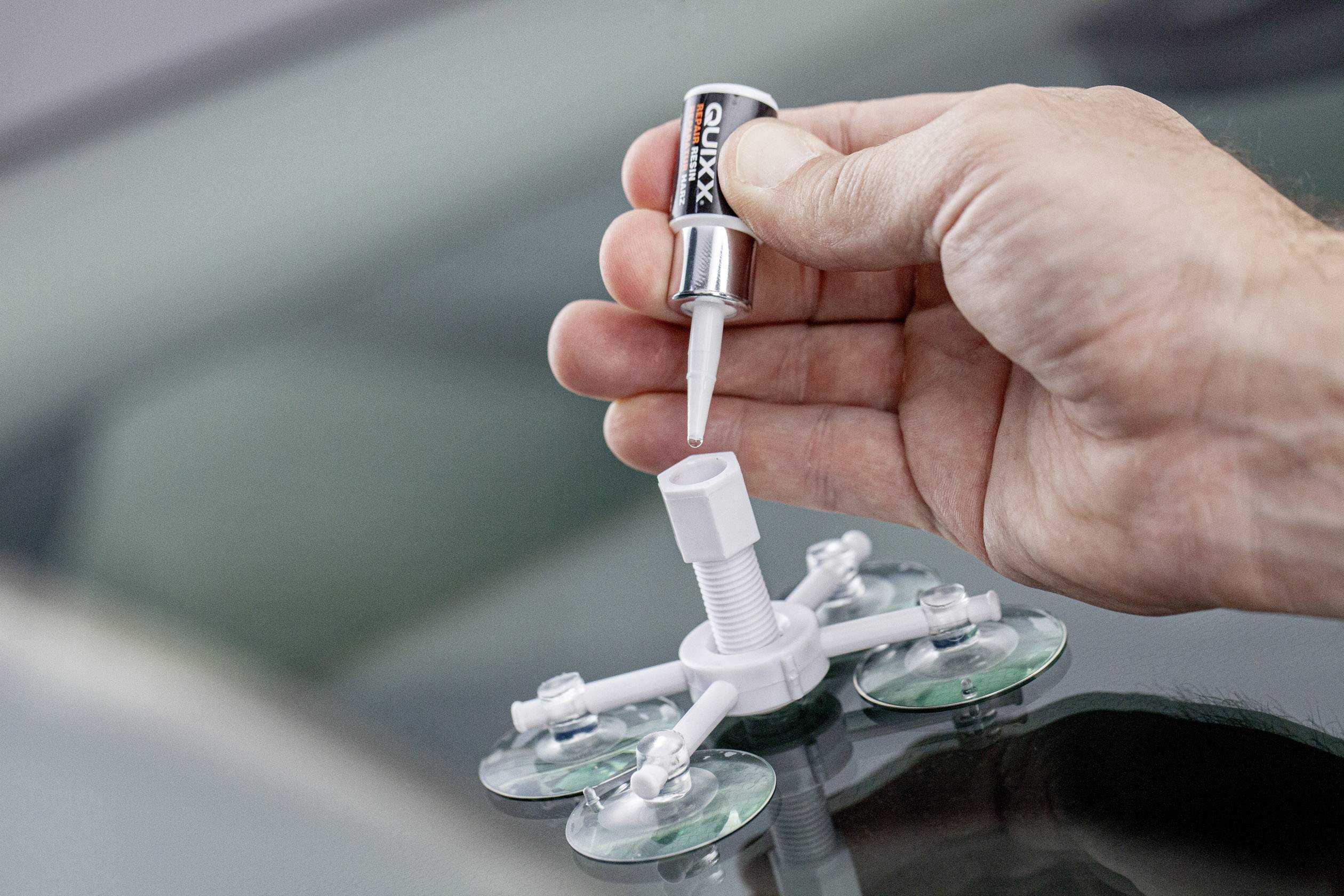 Eine Hand hält eine Tube Klebstoff über ein Reparaturwerkzeug mit Saugnäpfen für Autoglas, während Klebstoff hineingefüllt wird.