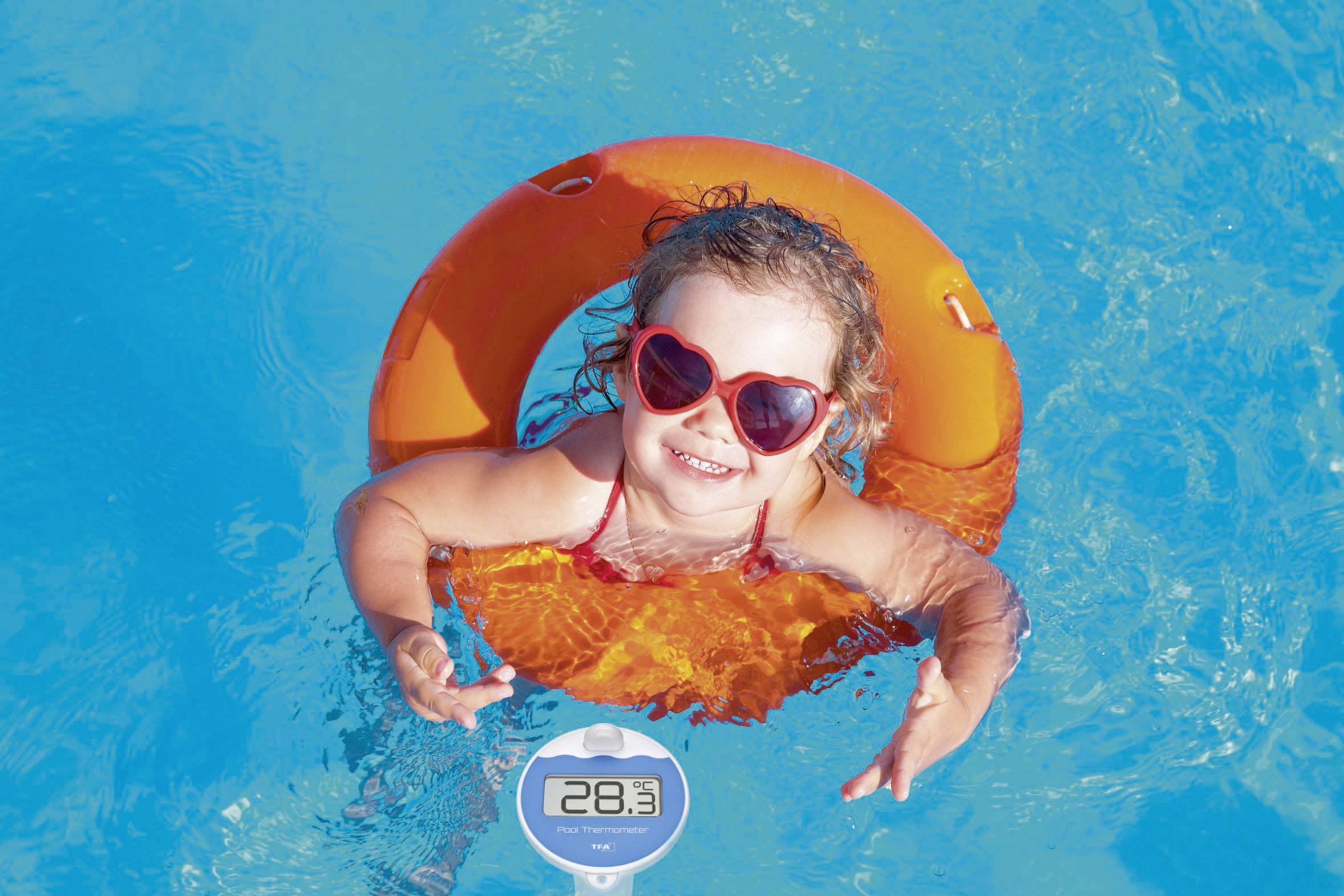 Kleines Kind mit roter Sonnenbrille schwimmt fröhlich in einem orangen Schwimmring im blauen Poolwasser. Temperaturanzeige zeigt 28,3°C.